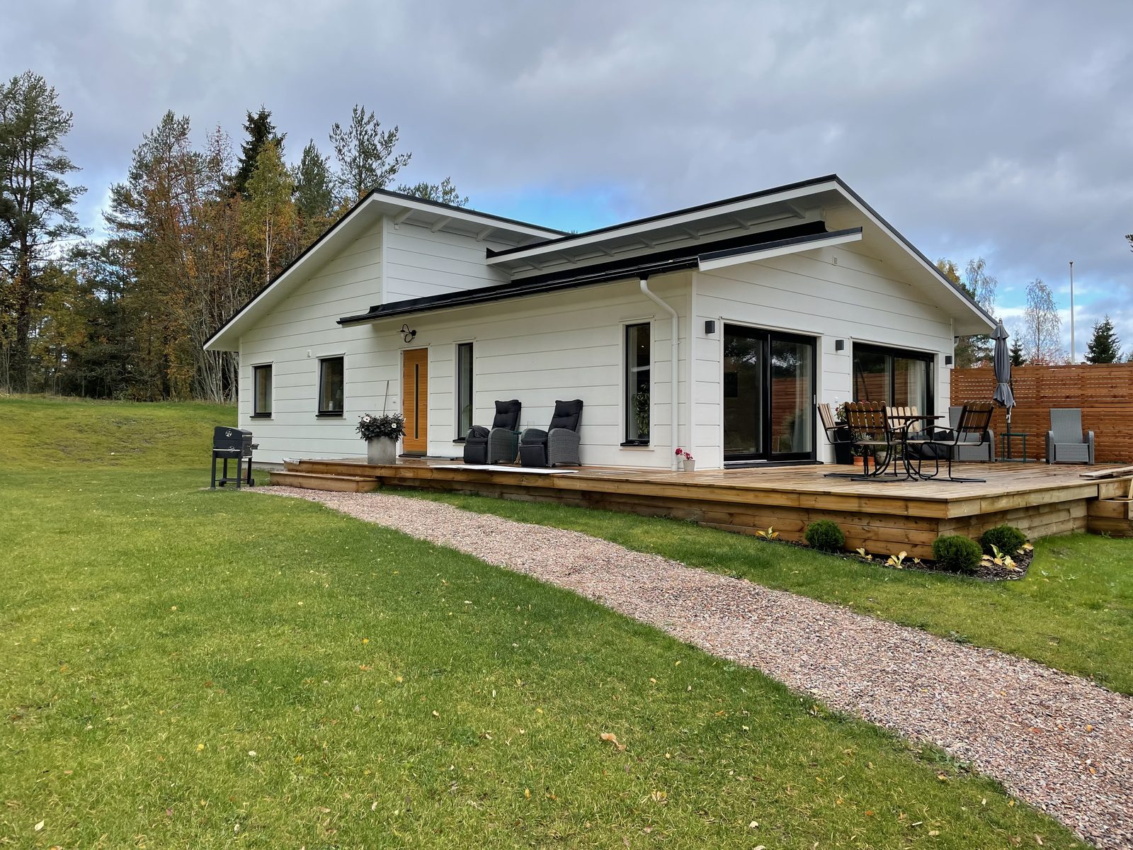 Vit enplansvilla med stort trädäck och grusgång över gräsmattan